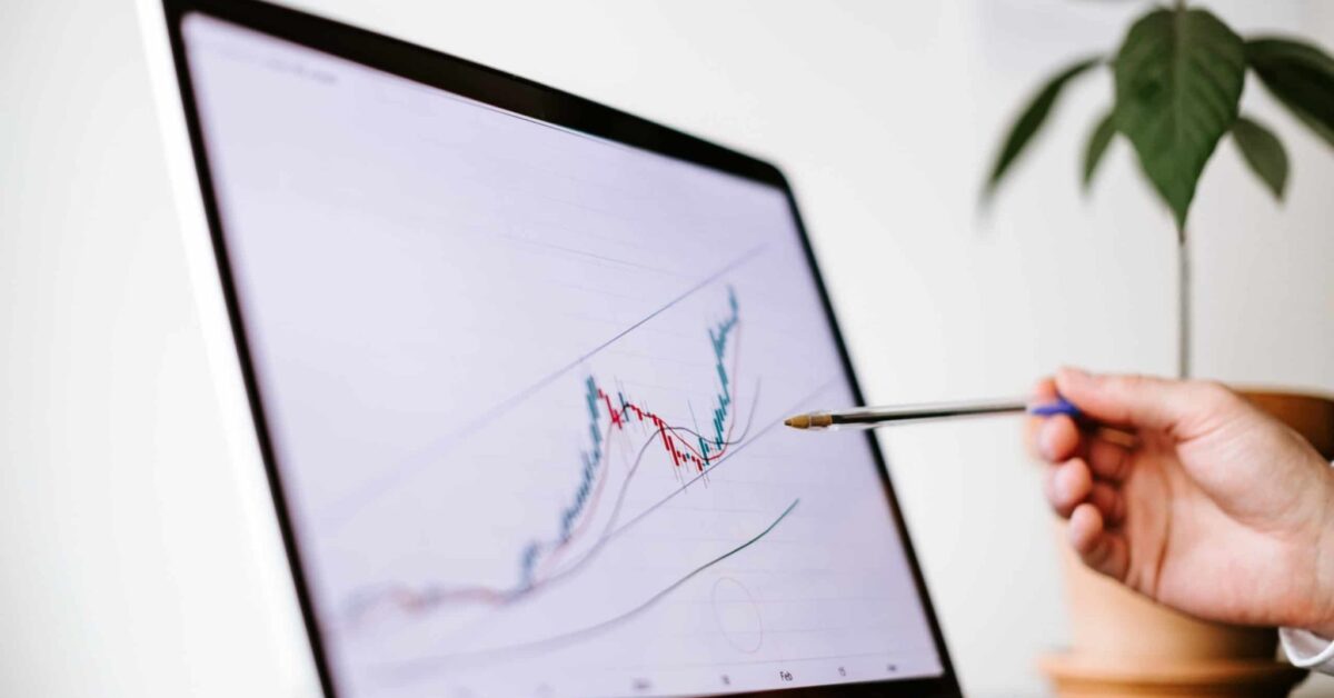 Someone holding a pen pointing at a computer screen showing a stock chart