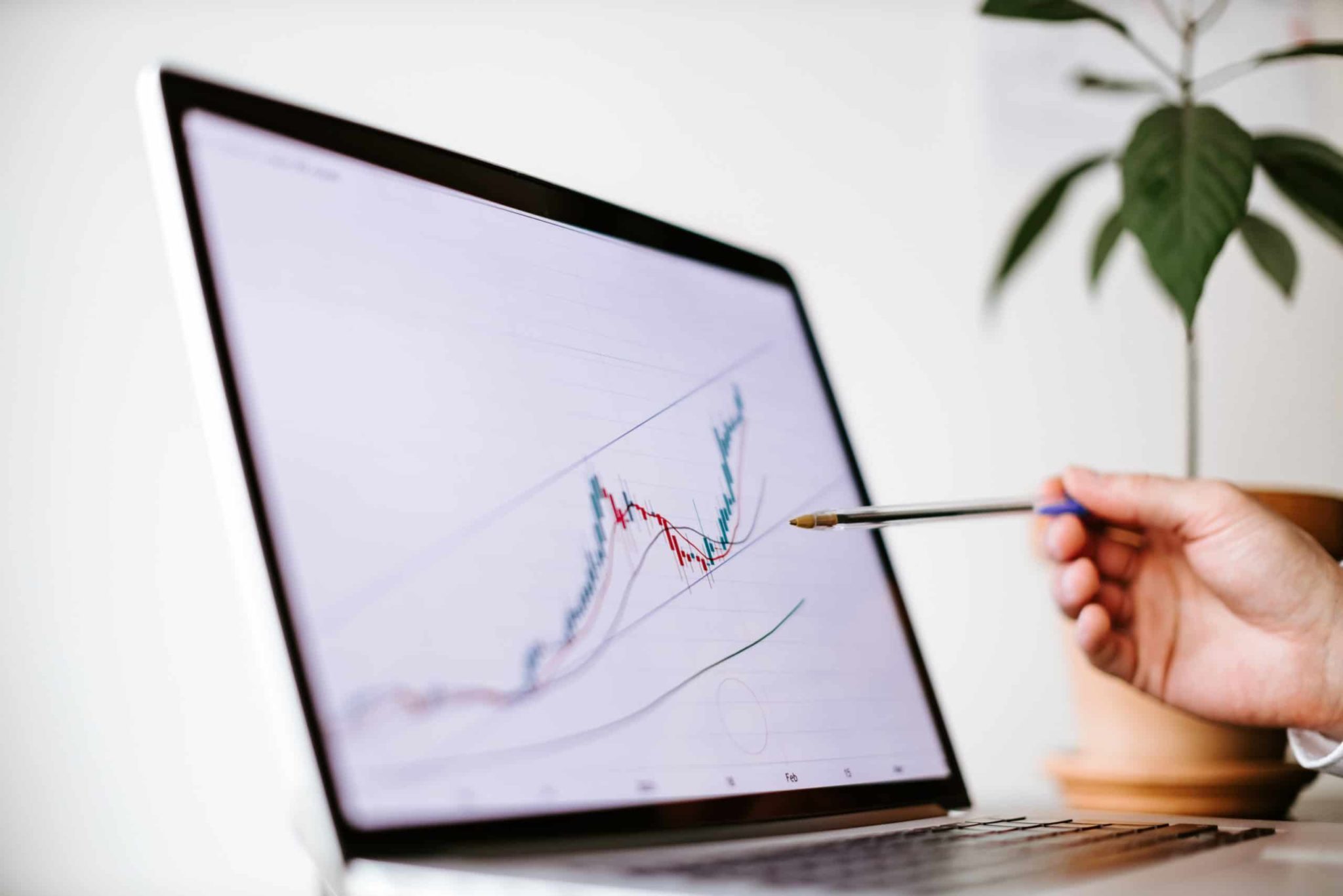 Someone holding a pen pointing at a computer screen showing a stock chart