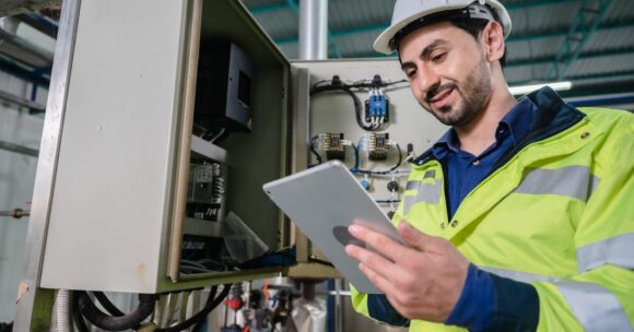 Technician reading tablet in front of electronics box