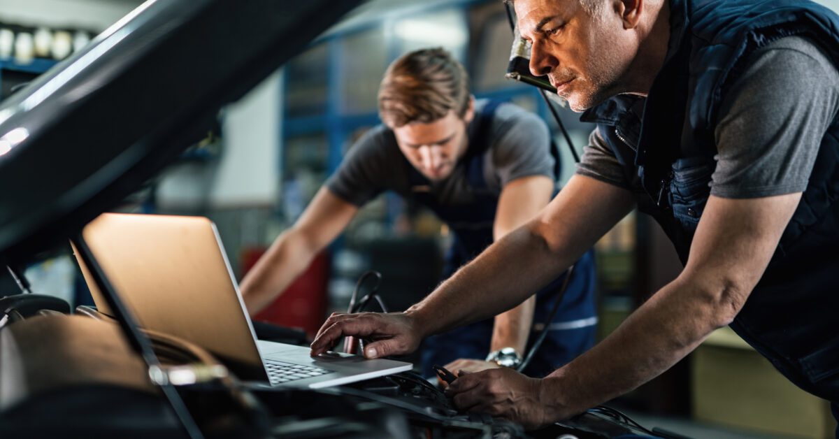 Mid adult mechanic using computer and doing car diagnostic with his coworker in auto repair shop.