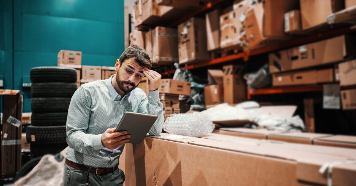 Hardworking businessman leaning on boxes in storage of shipping firm and checking on goods ready for shipment.